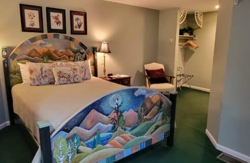 Pretty federal-style bedroom with bed, armoire, high-back davenport and pale-green walls with a floral wallpaper feature.
