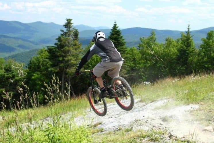 Man jumping a BMX bike over a hill surrounded by green hills and trees.