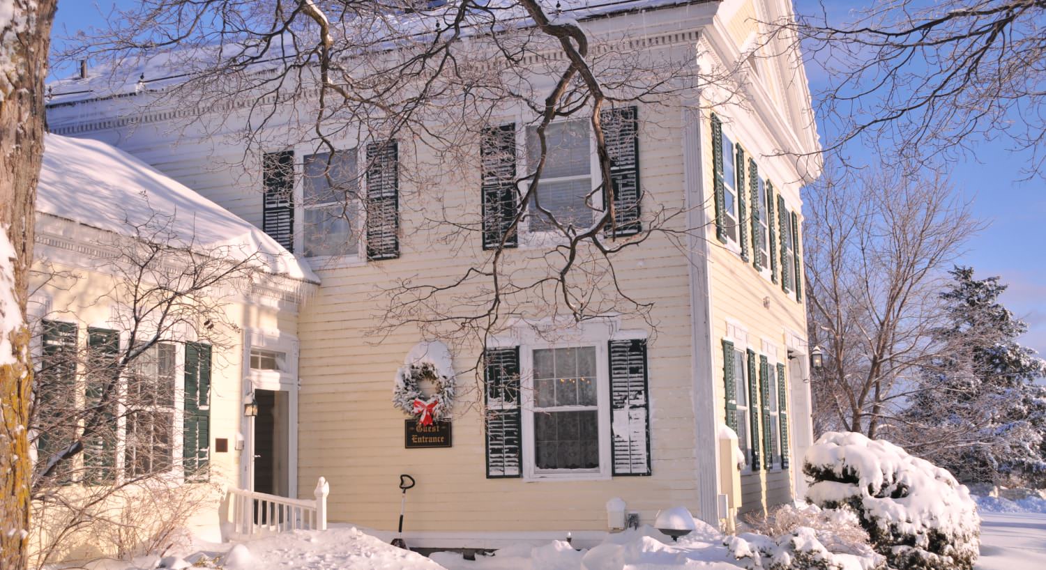 Exterior view of the property painted yellow with white trim and green shutters and covered in snow
