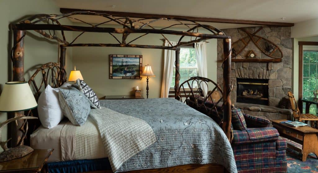 Beautiful rustic canopy bed made of branches with a blue coverlet in a bedroom with a stone fireplace.