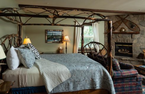 Beautiful rustic canopy bed made of branches with a blue coverlet in a bedroom with a stone fireplace.