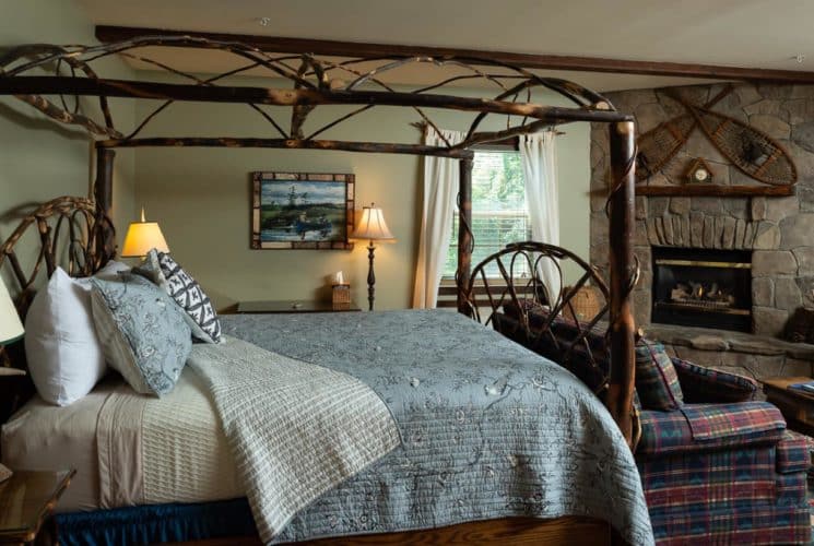Beautiful rustic canopy bed made of branches with a blue coverlet in a bedroom with a stone fireplace.