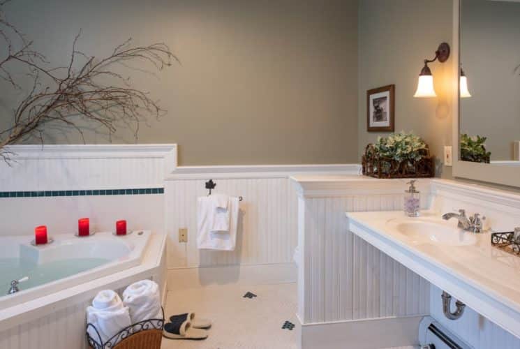 Corner spa tub in bathroom with tan walls and white wainscoting, tile floors, and a two-sink vanity.