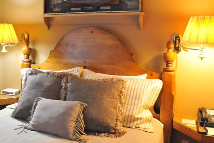 Twin wall lamps over side tables on either side of a wooden bed with beige linens and pillows.
