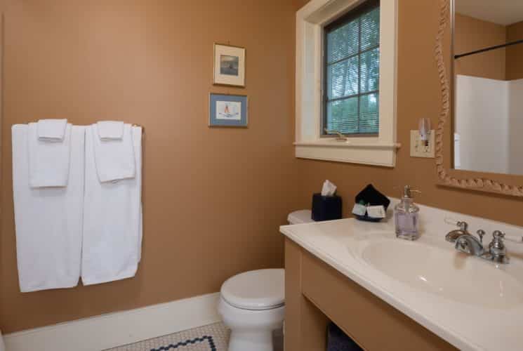 Bathroom with a built-in vanity and a large mirror, painted a dark tan with tile floor and white towels.