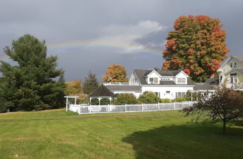 Large white house and green lawn under a beautiful rainbow in the sky.