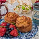 Two rolls on a blue and white plate with fruit next two two custom Deneen mugs with the Strong House Inn logo.