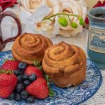 Two rolls on a blue and white plate with fruit next two two custom Deneen mugs with the Strong House Inn logo.