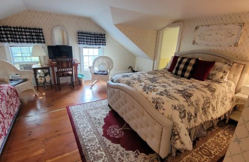 Cute bedroom with a couch, and bed with a padded headboard, red rug on wooden floors and wicker seating.