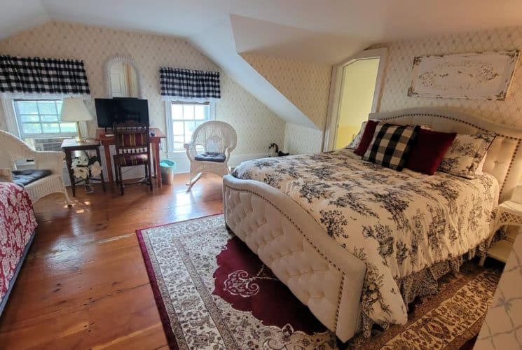 Cute bedroom with a couch, and bed with a padded headboard, red rug on wooden floors and wicker seating.