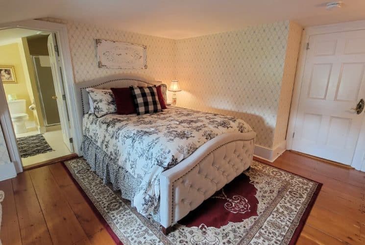 Cozy bedroom with a padded headboard on a comfy-looking bed, oriental carpet on wooden floor and pretty wallpaper.