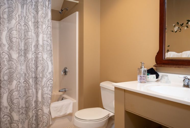 Bathroom with a built-in vanity and a large mirror, and shower and tub combo, painted tan with tile floor and white towels.