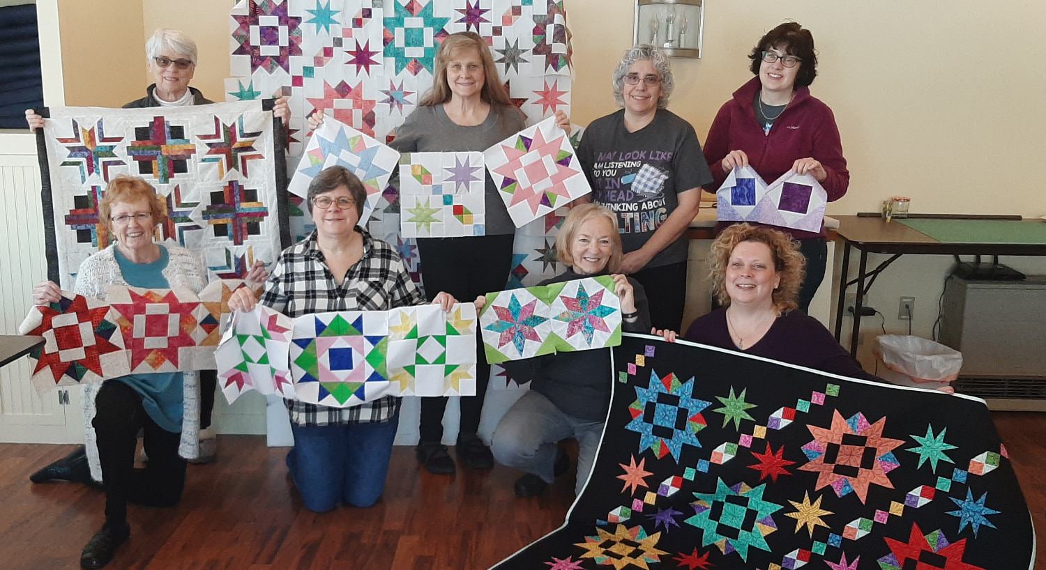 Group of ladies holding up multicolored quilts and individual quilt squares