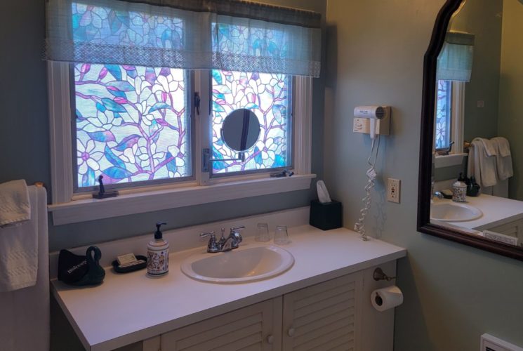 Vanity sink under stained-glass windows next to wooden-framed mirror in bathroom painted pale green.