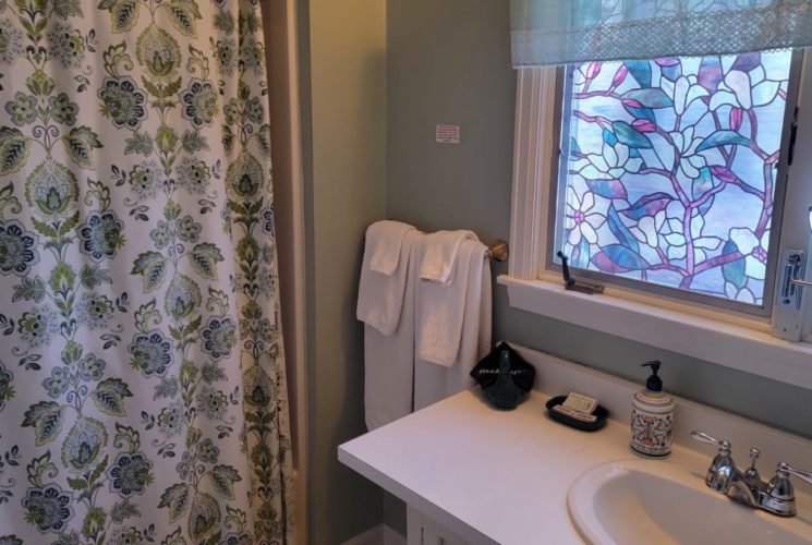 Bathroom vanity sink under stained-glass windows next to shower/tub combo with floral shower curtain.
