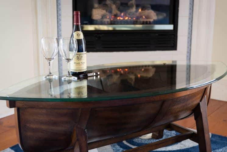 Interesting glass-topped canoe table with red wine bottle and two glasses in front of a fireplace.