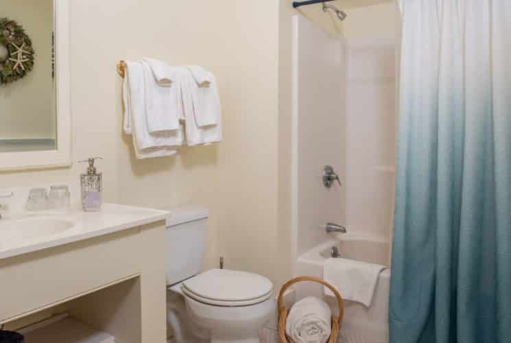 Bathroom painted cream with vanity sink and counter, mirror, tub/shower combo and white towels.