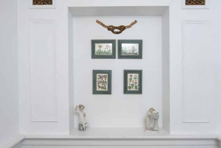Wall inset with three art pieces and 4 floral prints under two antique wall registers.