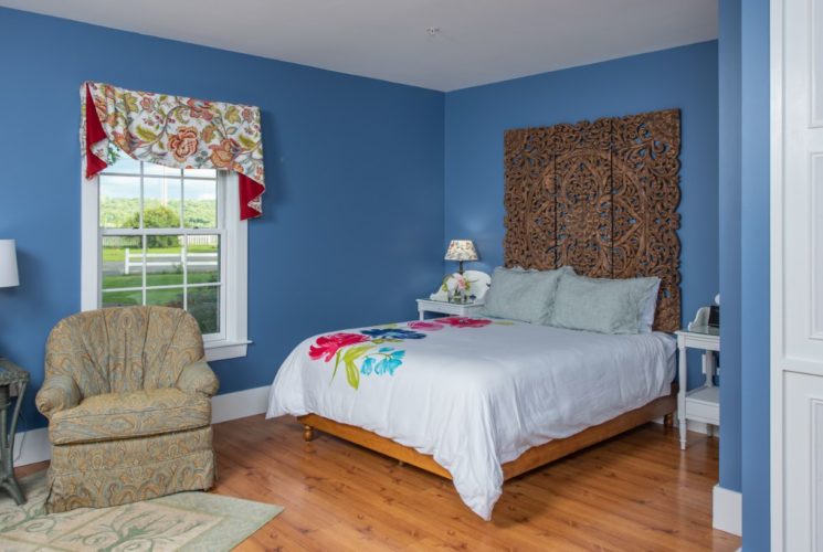 Pretty blue bedroom with a window, armchair and interesting wooden bed made up with a striking flowered duvet.