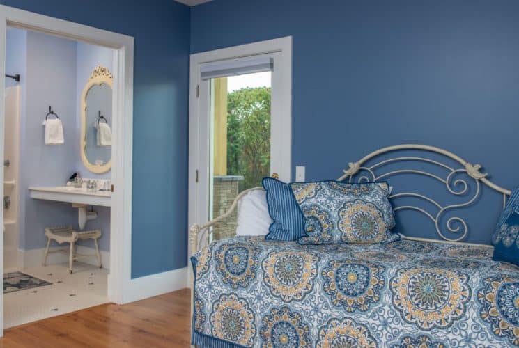 Pretty daybed with a blue and yellow quilt in a room painted blue with wooden floors, and an exterior glass door.