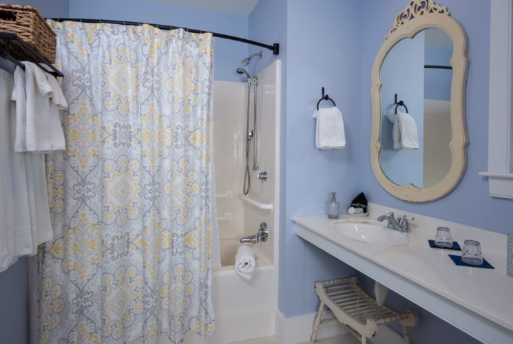 Pretty blue bathroom with tub/shower combo, White towels, long vanity and decorative mirror.