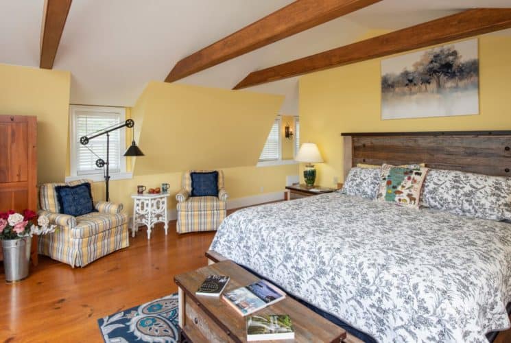 Yellow bedroom with wooden ceiling beams, modern wooden bed, seating area and a wooden screen.