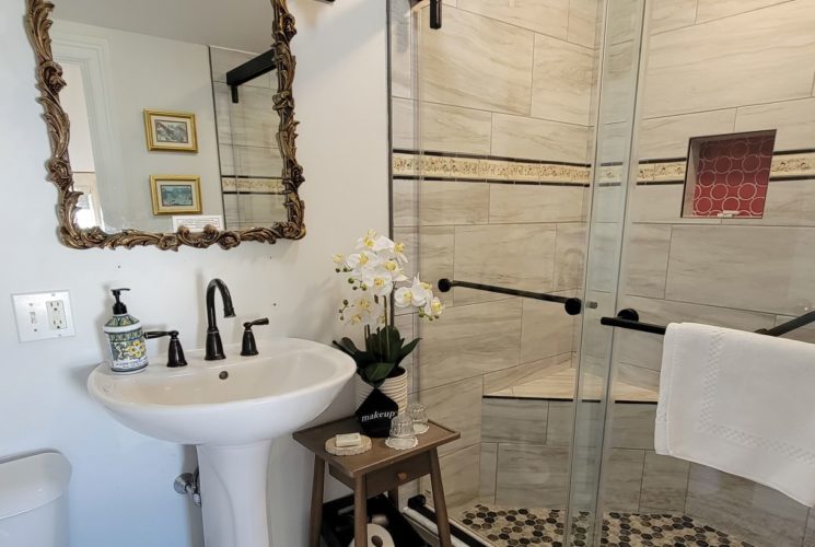 Modern glass shower enclosure with tiled walls and floor in bathroom with vanity sink and decorative mirror.