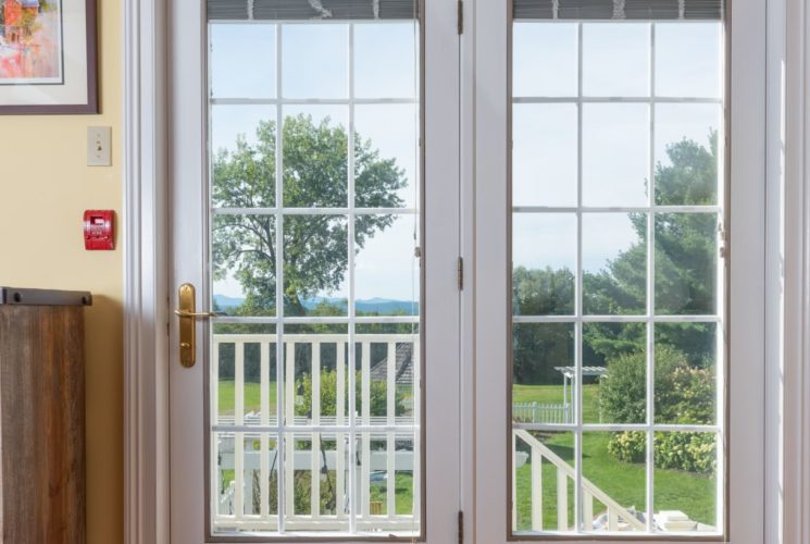 Wooden dresser in bedroom painted yellow with French doors leading out to pretty green lawn.W