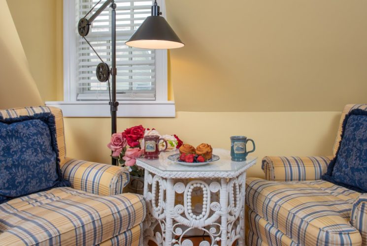 Seating area in pretty yellow bedroom with two blue and yellow plaid chairs and wicker table.