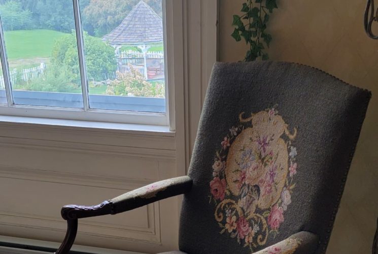 Needlepoint armchair in bedroom next to a window overlooking the gazebo.
