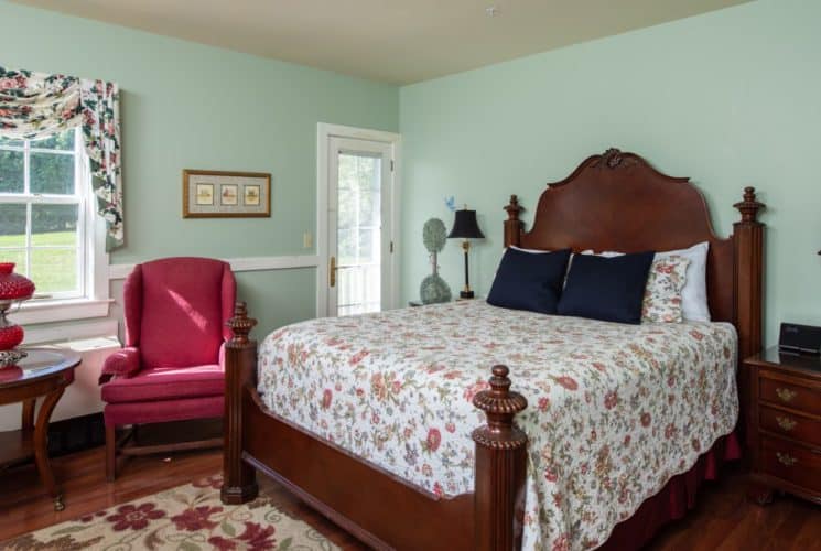 Bedroom painted pale green with dark Federal-style furniture and red and cream floor rug and coverlet on bed.