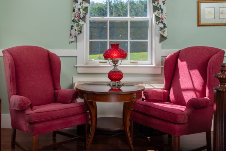 Elegant seating area with two red brocade chairs surrounding a wooden table with a red-glass converted oil lamp.