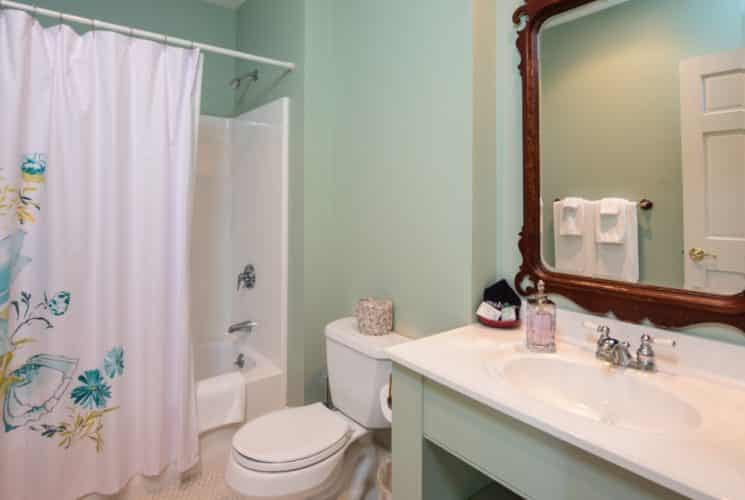 Pretty bathroom painted pale green with a tile floor, vanity, mirror, and tub/shower combo.