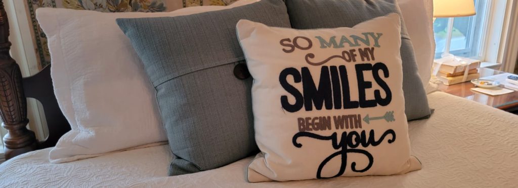 Decorative pillows on a cozy bed, cute pillow reading, "So many of my smiles begin with you".