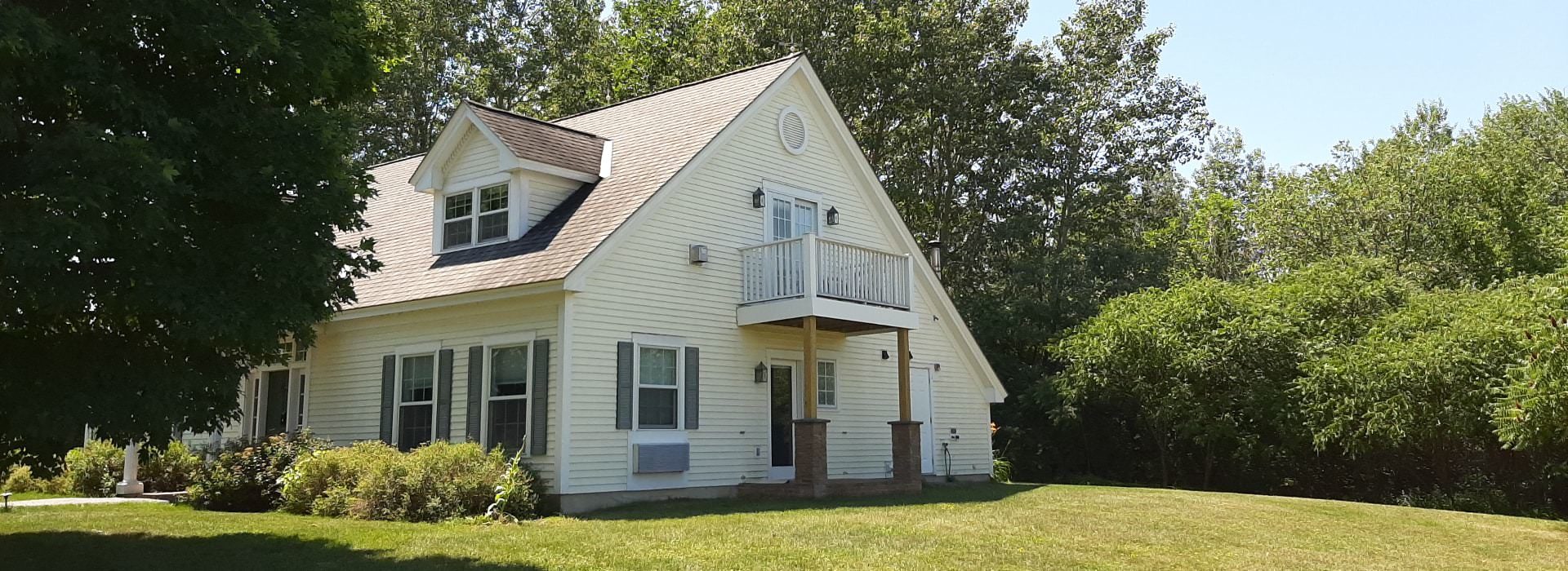 Adorable house with a sloped roof, windows with shutters and a balcony set among trees.