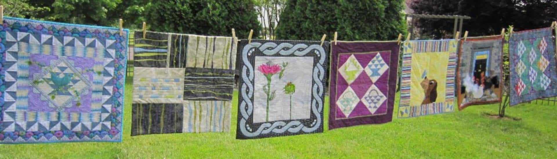 Seven beautiful hand-made quilts hanging on a clothes-line on a sunny day.