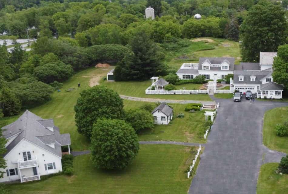 Overhead view of two large white houses with white fence, asphalt driveway and green lawn.