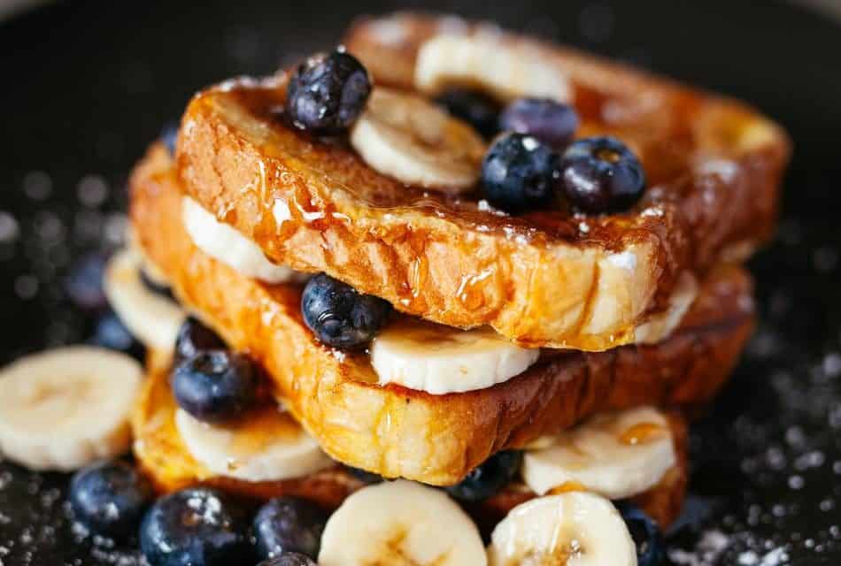 French toast layered with blueberries and bananas, dripping with syrup and sprinkled with powdered sugar.