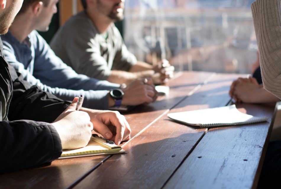 Four people sitting at a wooden table with notepads talking amongst themselves.