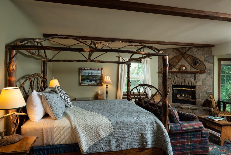 Beautiful rustic canopy bed made of branches with a blue coverlet in a bedroom with a stone fireplace.