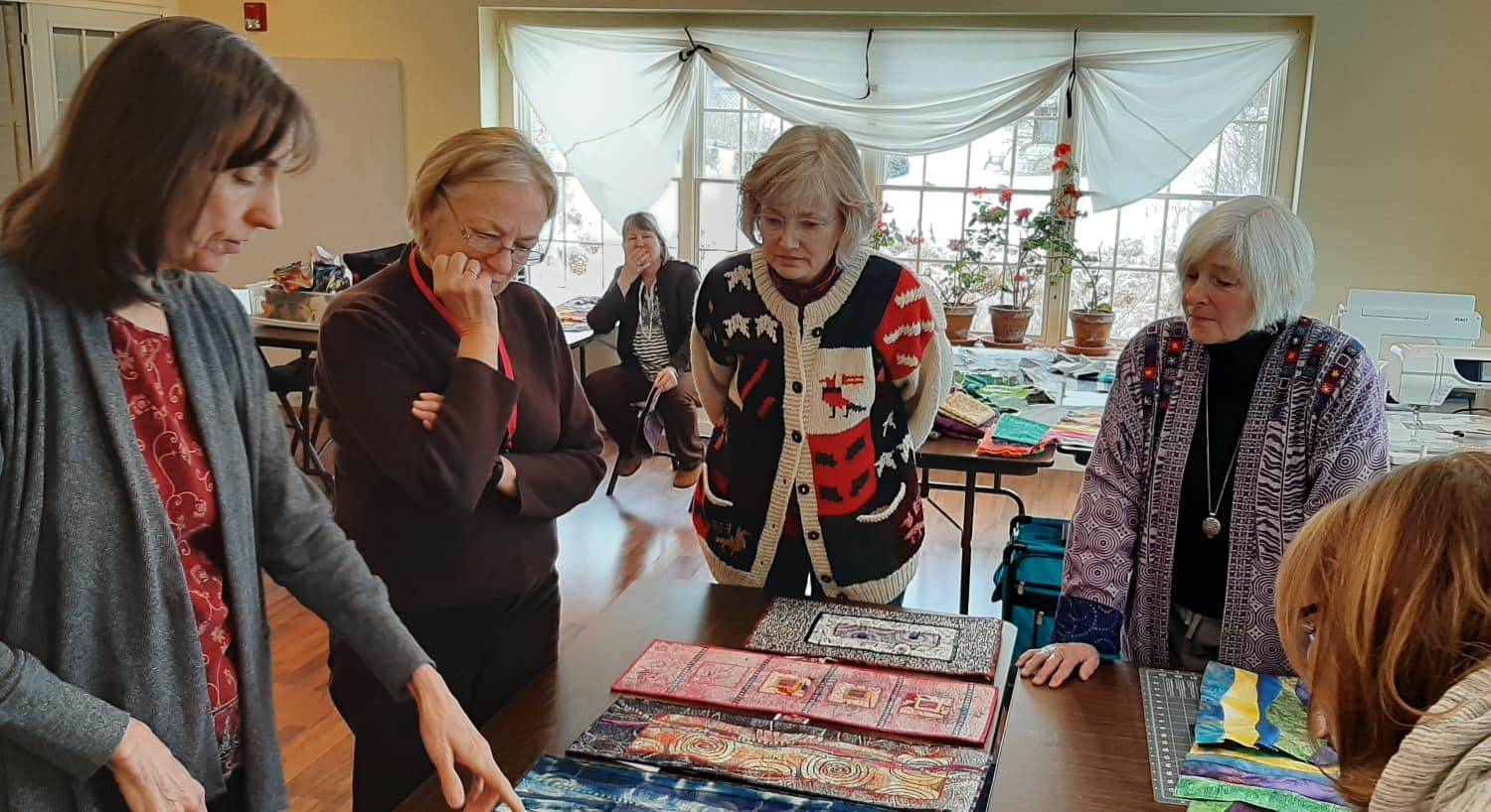 Ladies standing around table looking at multicolored quilting fabric