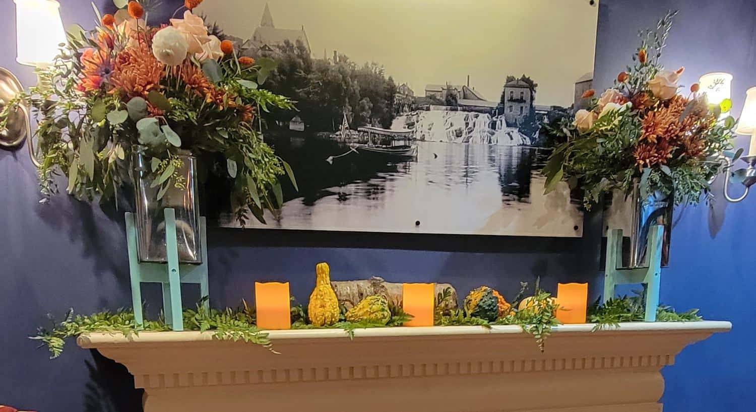 Fireplace mantel decorated with fall flowers, gourds, and candles