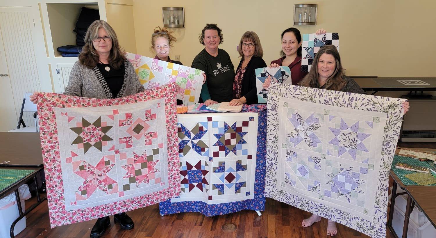 Group of ladies holding up multicolored quilts and individual quilt squares